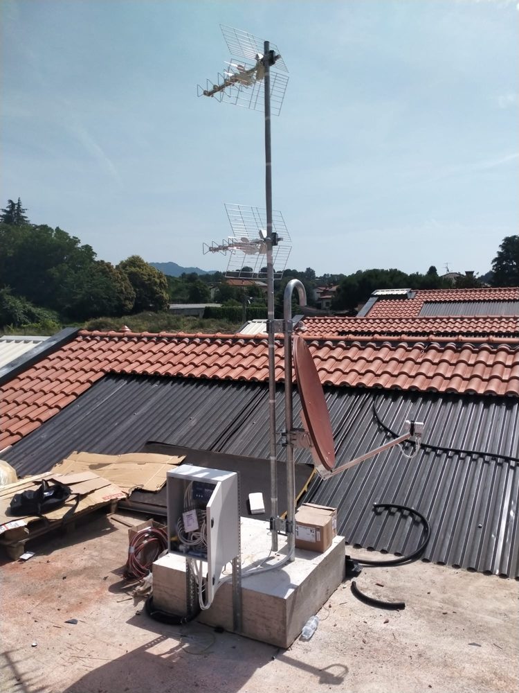Palo con antenne TV, parabola e quadro del centralino su un tetto piano