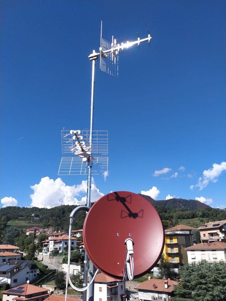 Palo con antenne TV e parabola rossa, con colline sullo sfondo